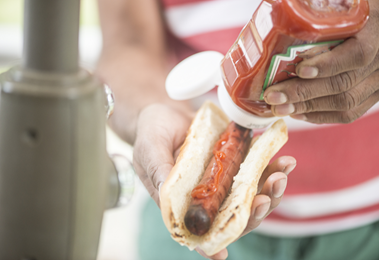A person puts ketchup on their hotdog.